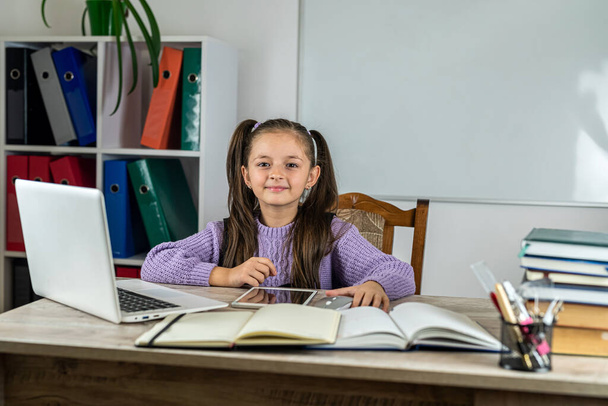 Retrato de uma menina bonita na sala de aula em uma mesa com livros e um computador. o conceito de aprendizagem. Escola. horário escolar - Foto, Imagem
