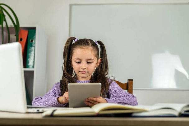 Retrato de una hermosa chica en el aula en un escritorio con libros y una computadora. el concepto de aprendizaje. la escuela. tiempo escolar - Foto, Imagen