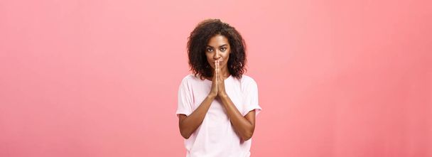 Créatif et intelligent élégant attrayant afro-américain femme avec coiffure bouclée ayant grand plan ou idée se sentant ambitieux tenant la main dans la prière sur la bouche regardant réfléchi à la caméra. Espace de copie - Photo, image