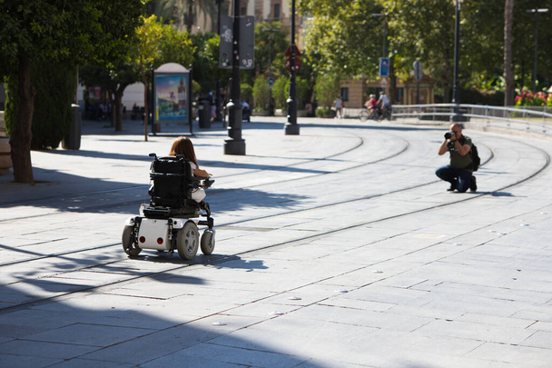 jovem deficiente em uma cadeira de rodas com mobilidade reduzida está posando para um fotógrafo que está fazendo uma sessão de fotos para uma agência para modelos com deficiência. - Foto, Imagem