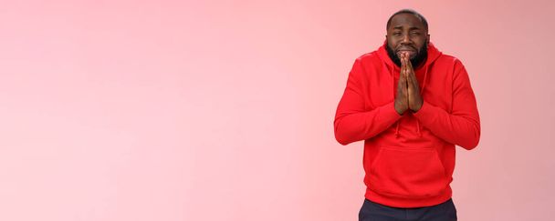 Miserabele Afro-Amerikaanse man baard in rode hoodie bukken maken smeken boos grimas grijnzen snikken vragen hulp zeggen houd elkaars hand bidden genade, verontschuldigen geld nodig. - Foto, afbeelding