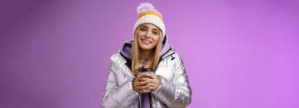 Tender relaxed cheerful smiling blond girl look pleased relieved drinking hot coffee cacao enjoying nice heartwarming moment look camera delighted gentle grin, wearing winter jacket hat. - Photo, Image