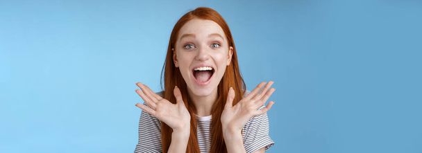 Happy cheerful rejoicing young pretty redhead supportive girlfriend clasp hands joyfully yelling congratulations raising hands amused wide eyes surprised getting awesome good news, blue background. - Photo, Image