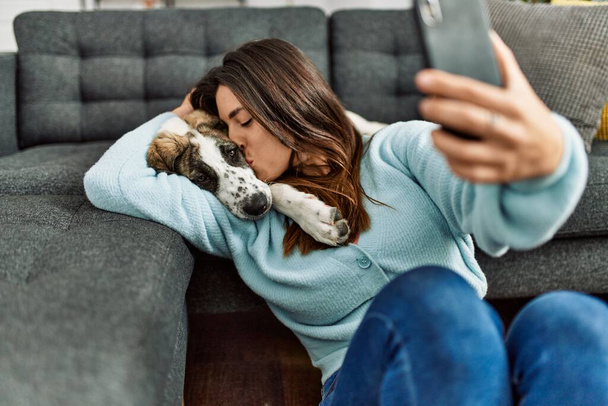 Mujer joven besando y abrazando perro haciendo selfie por el teléfono inteligente en casa - Foto, imagen