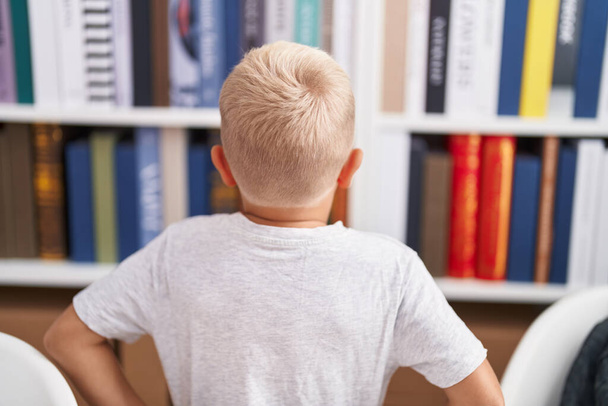 Adorable toddler looking for book of shelving at classroom - Photo, Image