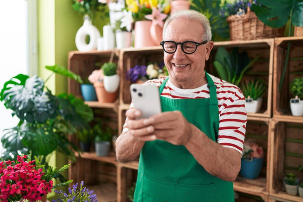 中年白髪の男花屋笑顔自信を持って使用してスマートフォンに花店 - 写真・画像