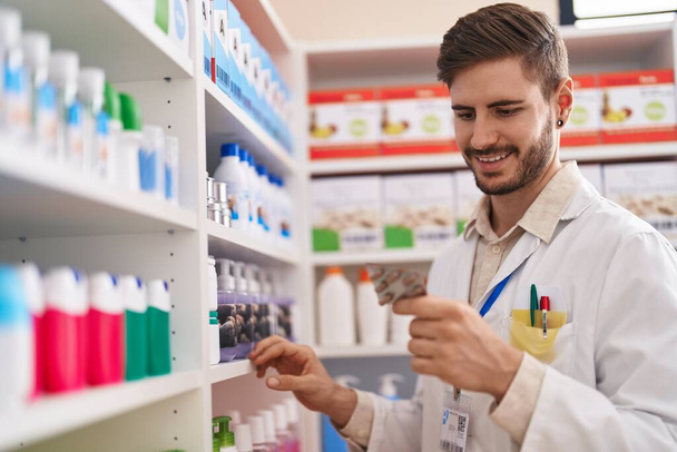 Молодий кавказький чоловік фармацевт тримає таблетки стелажів в аптеці
 - Фото, зображення