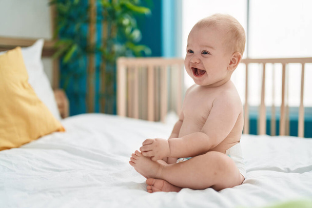 Adorable bébé caucasien souriant confiant assis sur le lit dans la chambre - Photo, image