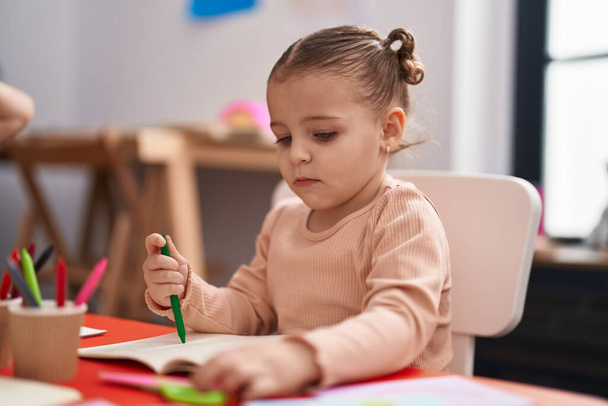 Adorable estudiante hispana sentada en la mesa dibujando sobre papel en el jardín de infantes - Foto, imagen