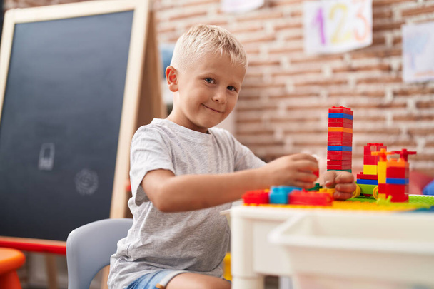 Adorable toddler playing with construction blocks sitting on table at classroom - Fotoğraf, Görsel