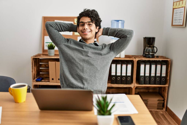 Nuori latino liikemies rentouttava kädet pään päällä toimistossa. - Valokuva, kuva