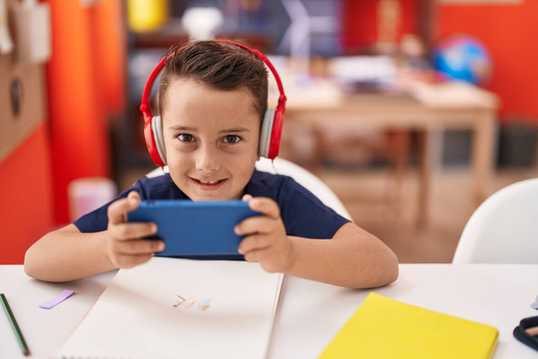 Suloinen latino lapsi opiskelija käyttää älypuhelin ja kuulokkeet opiskelu luokkahuoneessa - Valokuva, kuva