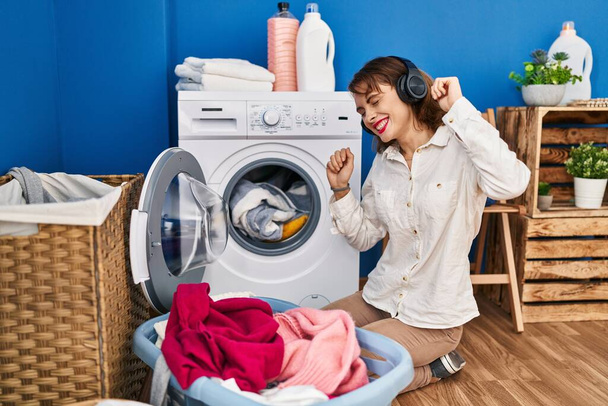 Νεαρή καυκάσια γυναίκα που ακούει μουσική περιμένοντας το πλυντήριο - Φωτογραφία, εικόνα