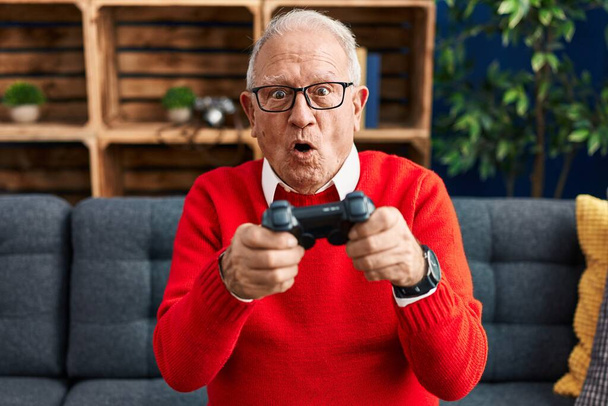 Старший мужчина играет в видеоигры сидя дома на диване - Фото, изображение