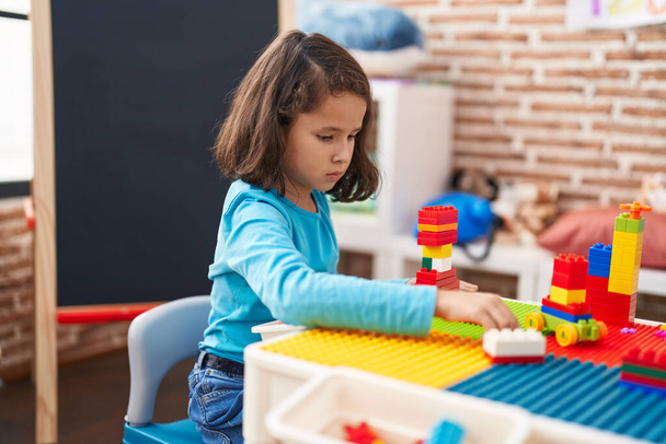 Adorable chica china jugando con bloques de construcción sentado en la mesa en el jardín de infantes - Foto, imagen
