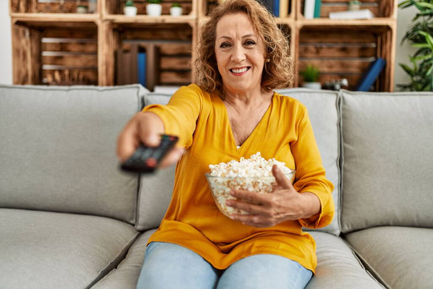 Middle age caucasian woman watching movie sitting on the sofa at home. - Zdjęcie, obraz