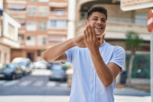 Νεαρός Ισπανός χαμογελαστός με αυτοπεποίθηση ξοδεύει χρήματα στο δρόμο. - Φωτογραφία, εικόνα