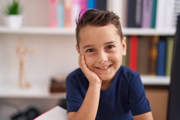 Sevimli İspanyol çocuk kütüphane okulundaki masada kendinden emin bir şekilde gülümsüyor. - Fotoğraf, Görsel