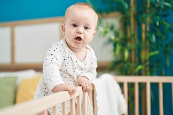 Adorable caucasian baby standing on cradle at bedroom - Photo, Image
