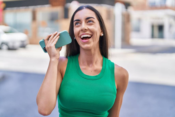 Giovane bella donna ispanica sorridente fiducioso messaggio audio di ascolto dallo smartphone in strada - Foto, immagini