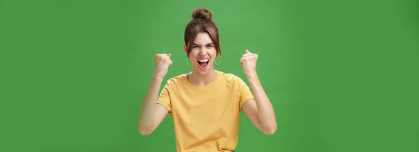 Zuřivá a mocná dobře vypadající emotivní žena ve žlutém tričku se zaťatými zuby řvoucí v jásotu oddaný fanoušek, podporující oblíbený tým, který chce vyhrát zvednutím zaťatých pěstí ve vítězství - Fotografie, Obrázek