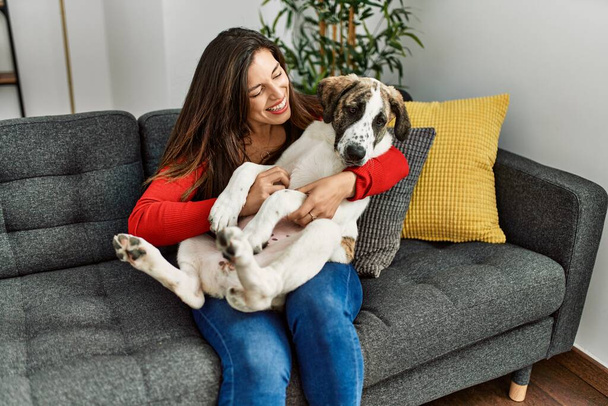 Młoda kobieta przytula psa siedząc na kanapie w domu - Zdjęcie, obraz