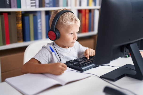 Adorable toddler student using computer writing on notebook at classroom - Photo, Image