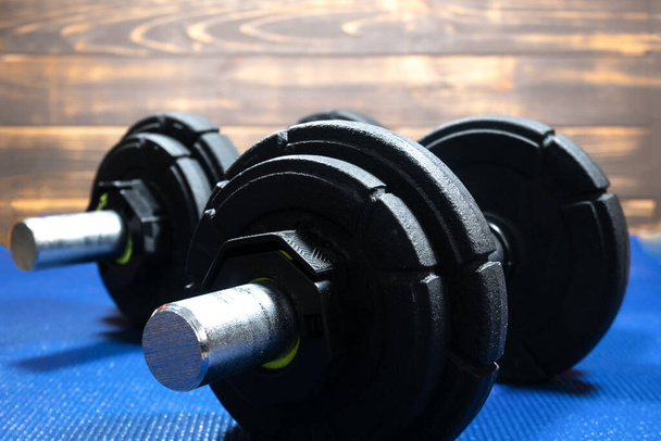 Heavy black dumbbells lying on the sports mat in the gym. Fitness sport motivation. Happy healthy lifestyle living. Exercises with bars weights. Home sport training. - Photo, Image