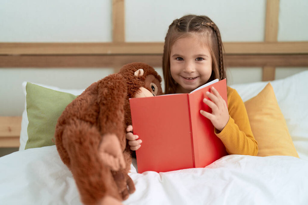 Adorabile libro di lettura ispanica ragazza seduta sul letto in camera da letto - Foto, immagini