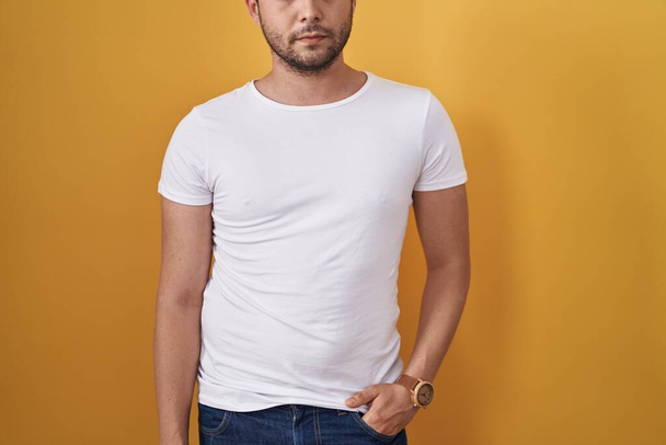 Hispanic man wearing white t shirt over yellow background thinking attitude and sober expression looking self confident  - Photo, Image
