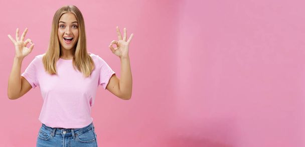 Портрет захопленої привабливої кавказької дівчини в модній футболці і джинсах, що показують добре або підтверджують жест з розважальною широкою посмішкою, що стоїть задоволений рожевим фоном, реагуючи на відмінні новини
 - Фото, зображення