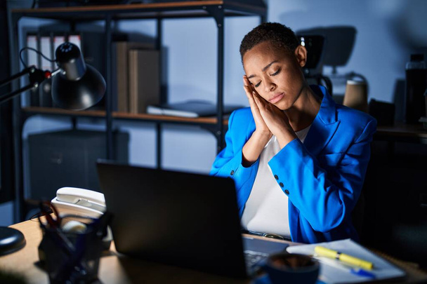 Kaunis afrikkalainen amerikkalainen nainen työskentelee toimistossa yöllä nukkuu väsynyt haaveilee ja poseeraa kädet yhdessä hymyillen suljetuin silmin.  - Valokuva, kuva