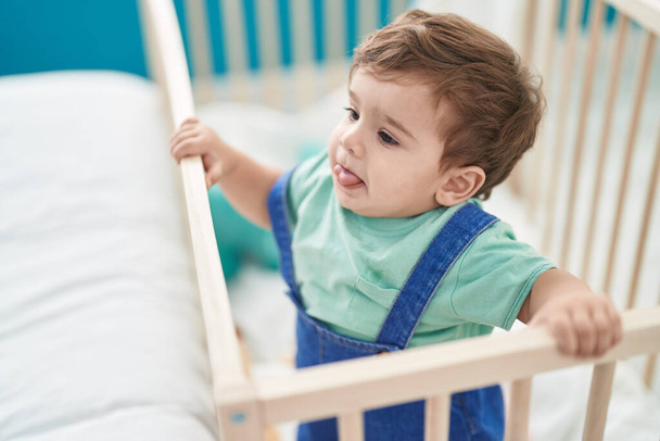 Adorable hispanic toddler standing on cradle at bedroom - Foto, afbeelding