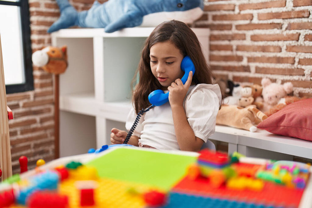 Liebenswertes hispanisches Mädchen spielt im Kindergarten mit Telefonspielzeug am Tisch - Foto, Bild