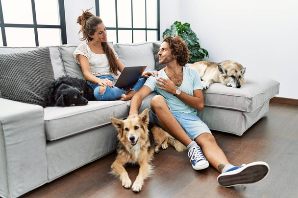 Jovem casal hispânico com cães relaxando em casa sorrindo olhando para o lado e olhando para longe pensando.  - Foto, Imagem