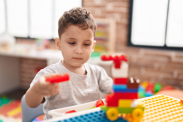 Adorable hispanic toddler playing with construction blocks sitting on table at kindergarten - Photo, image