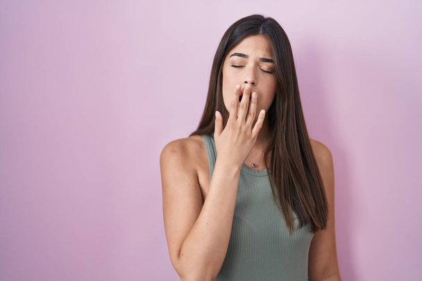 Hispanic woman standing over pink background bored yawning tired covering mouth with hand. restless and sleepiness.  - Photo, Image