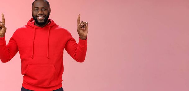 Devious cute african-american bearded guy in red hoodie smiling mysterious know exactly what you want pointing raised index fingers up grinning show perfect copy space promo, pink background. - Photo, Image
