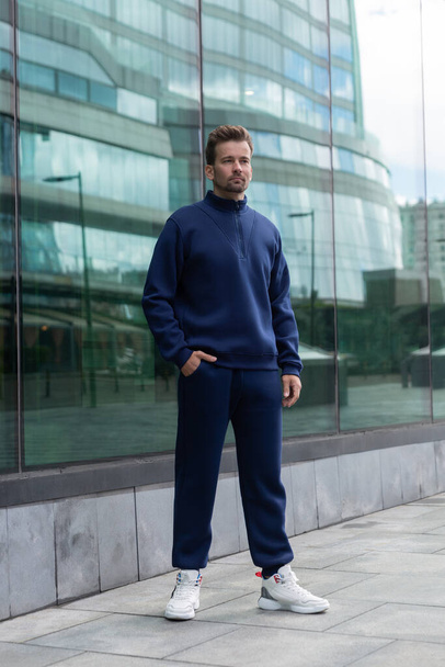 Full-length young man wears a vinous sports suit and poses for the camera. Athletic handsome young man stands on urban location and shows sports suit. Mock-up - Fotografie, Obrázek