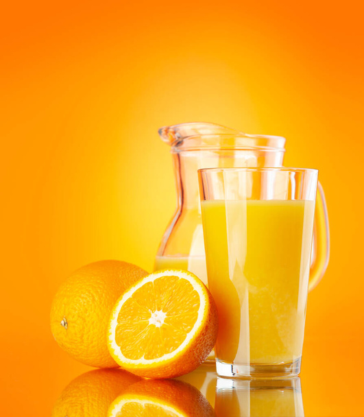 Čerstvý pomerančový džus ve skleněném džbánu přes oranžové pozadí - Fotografie, Obrázek
