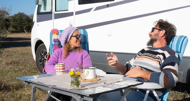 Muž a žena baví a relaxovat spolu před jejich karavan auto sedí u stolu a mluví spolu se smíchem. Šťastné turisty těšit cestovní životní styl a dovolenou na cestách - Fotografie, Obrázek