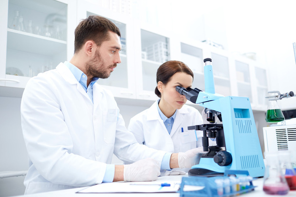 scientists with clipboard and microscope in lab - Photo, Image