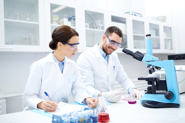 scientists with clipboard and microscope in lab - Photo, image