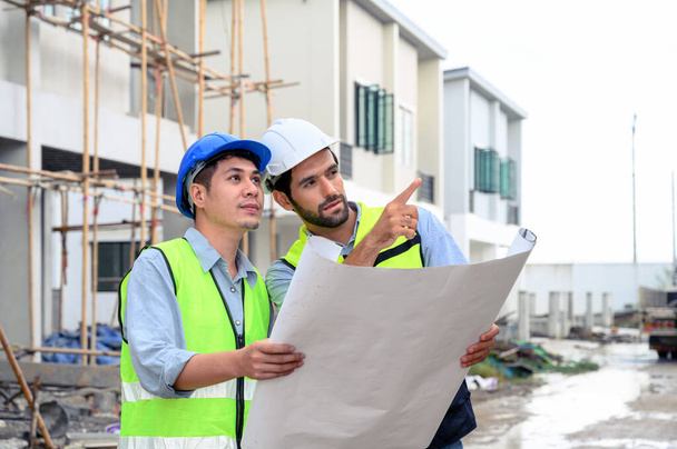 Construction engineer and architect check plan working with the blueprint on construction site. They are in safety vests with helmets for safety. Construction project concept - Foto, Imagem