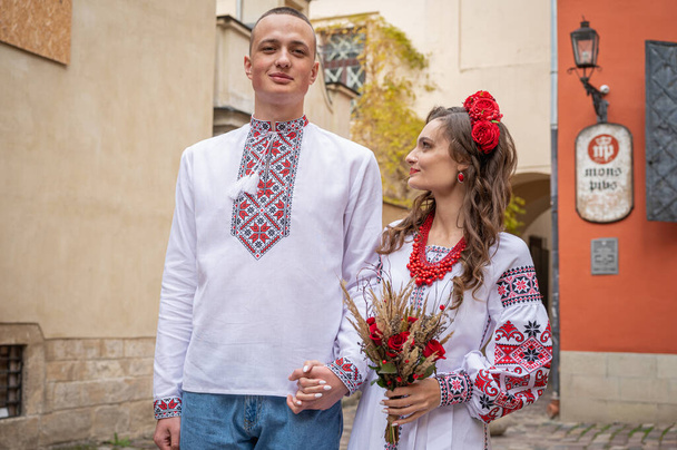 Birbirine aşık genç bir çiftin portresi, eski şehir Lviv 'de geleneksel Ukrayna gömlekleriyle yürüyen, el ele tutuşan bir aile. Gençler eski Lviv kasabasında sarılıyor - Fotoğraf, Görsel