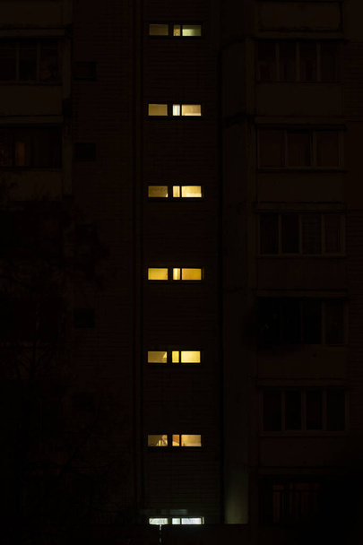 Una fila verticale di strette finestre rettangolari di un grattacielo residenziale brilla al buio. Sembra un indicatore della batteria.. - Foto, immagini