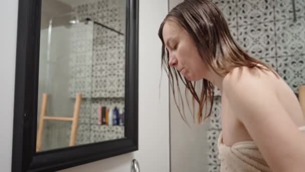 Havluya sarılmış bir kadın saç fırçasıyla saçını tarar ve banyoda saç kurutma makinesiyle kurutur. Kadın sabah hijyeni ve saç bakımı - Video, Çekim