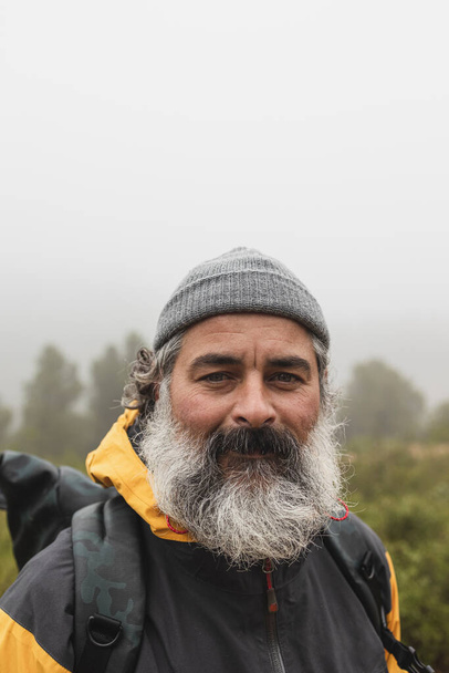 Bulutlu bir parkta kendine güvenen sakallı bir adam portresi. Yakışıklı sakallı hippi ormanda yürüyüş yapıyor.. - Fotoğraf, Görsel