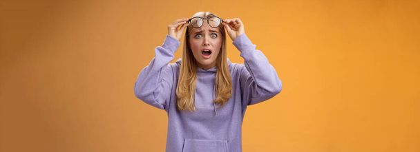 Σοκαρισμένη νεαρή γυναίκα που φαίνεται φοιτήτρια καταστρέφει τη δουλειά της κοιτάζοντας διαταραγμένα αναστατωμένα γυαλιά απογειώσεων που αναβοσβήνουν τα μάτια της κάμερας λαχανιάζοντας άφωνο τρομερό ατύχημα συνέβη, πορτοκαλί φόντο. - Φωτογραφία, εικόνα