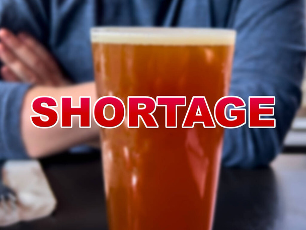 Blurred background of a glass of beer with the word Shortage in the foreground - Photo, Image
